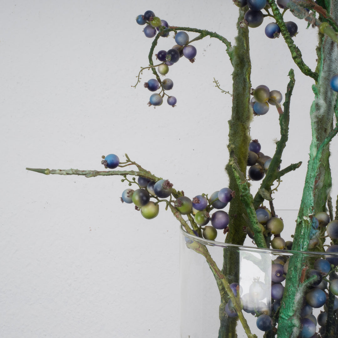 Large glass vase with beautiful branches of fake eucalyptus fruits in blue and green